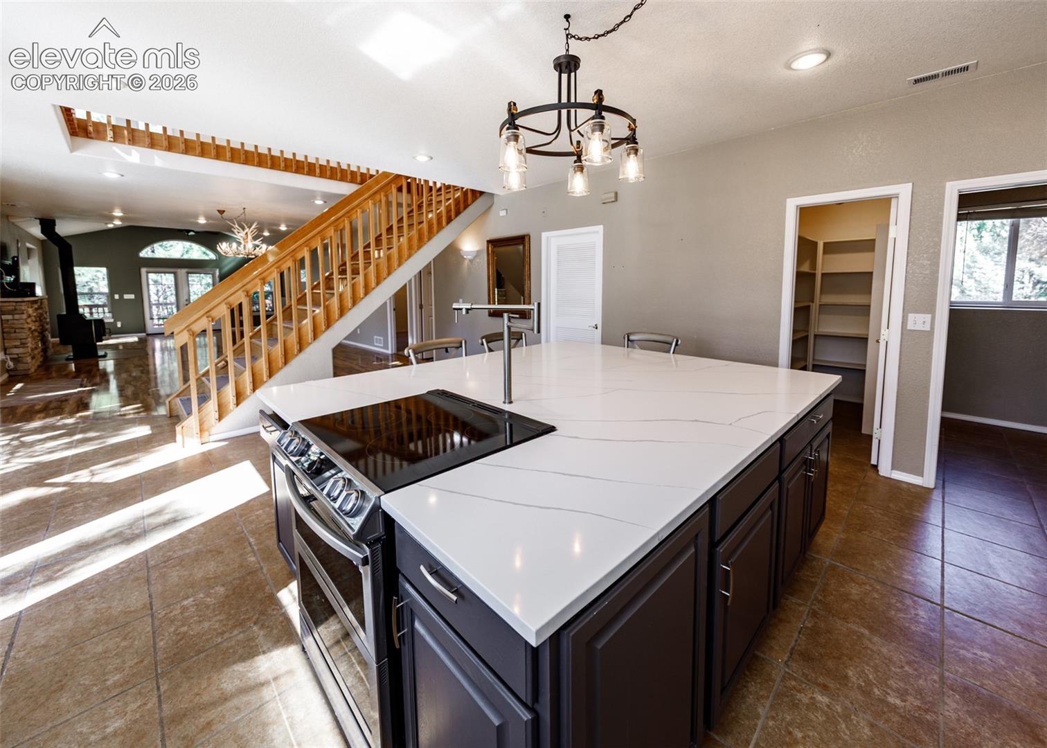 Kitchen island featuring a white surface with grey veining, dark-toned cabinetry, a built-in cooktop, and a metal faucet