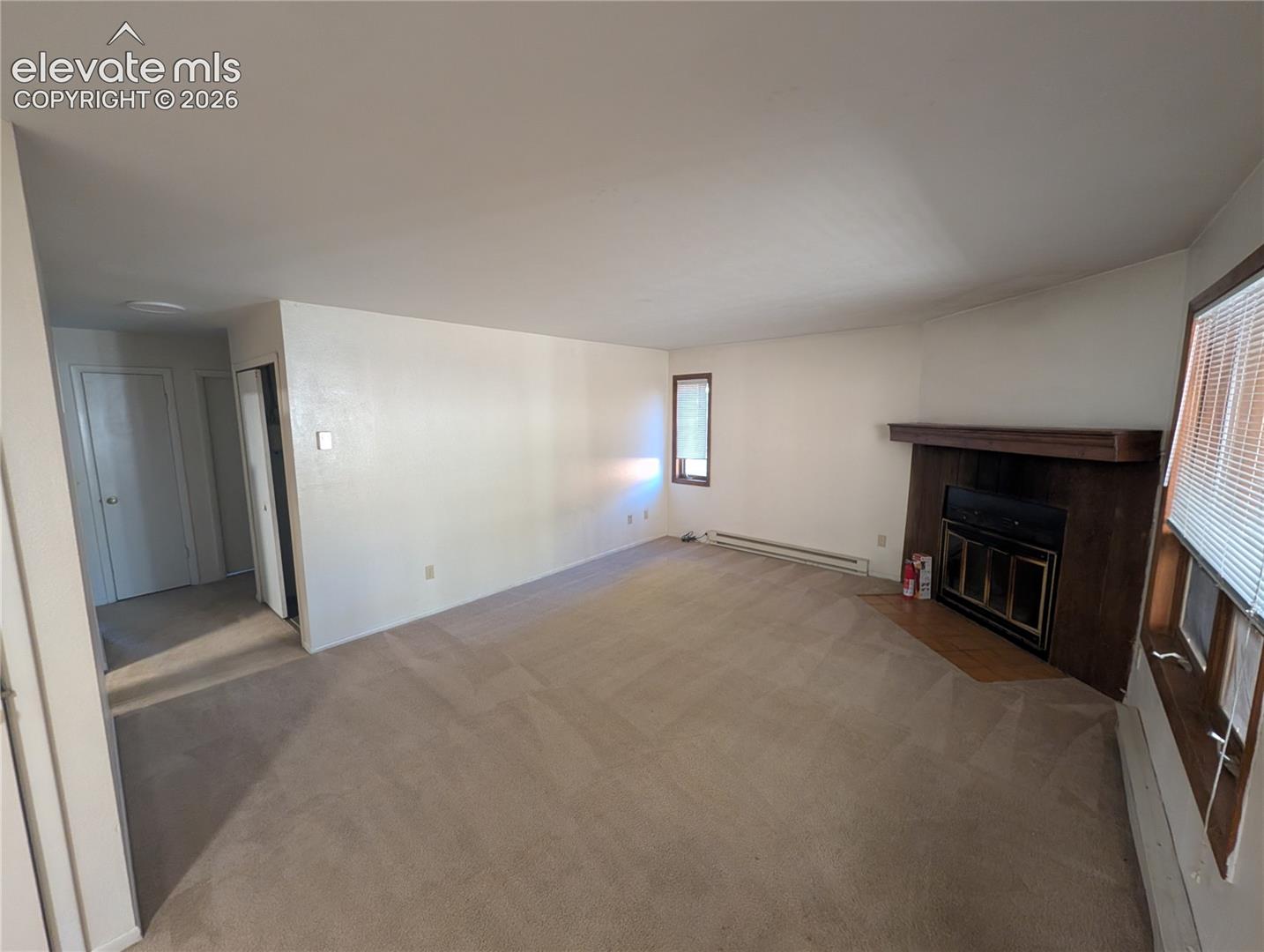 Expansive living area featuring neutral carpeting, a built-in fireplace with a wood mantel, and multiple windows with blinds