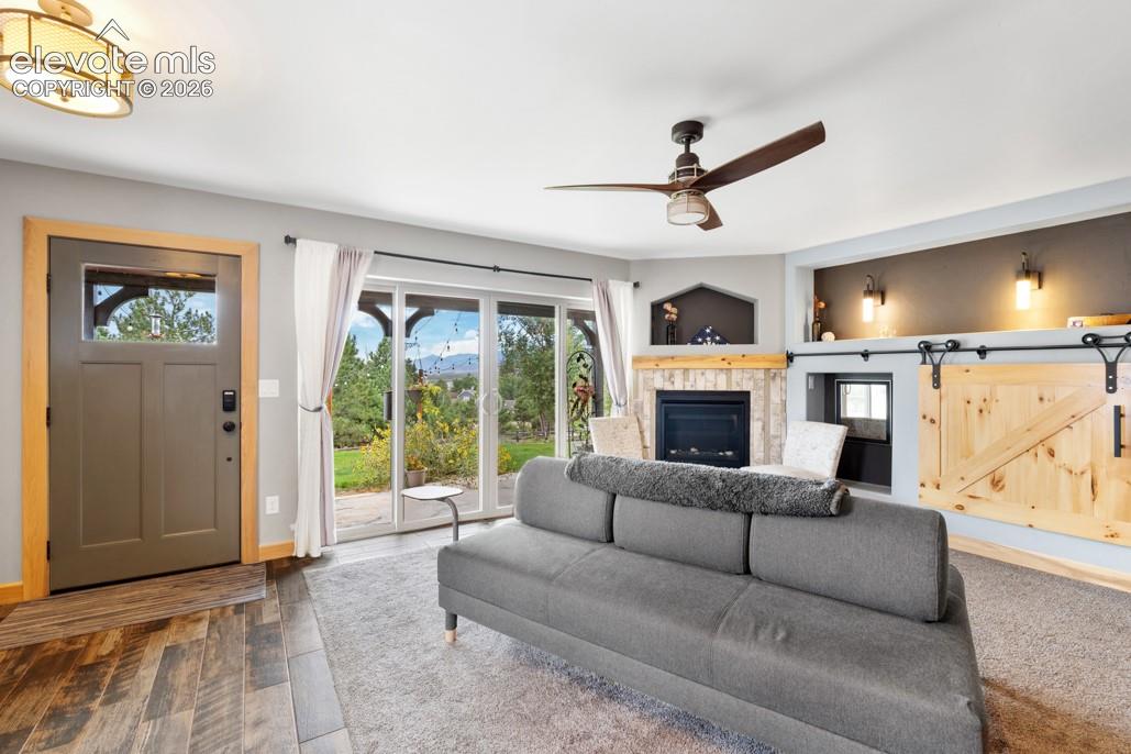Wood-finish flooring, sliding glass doors to the exterior, built-in fireplace with stone surround, ceiling fan, and built-in storage with barn doors