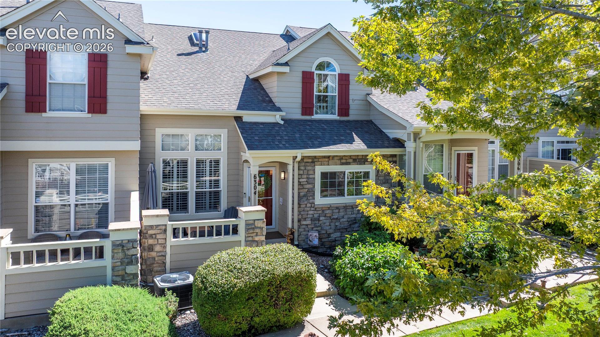 Multi-level exterior featuring stone veneer accents, lap siding, decorative shutter detailing, gabled rooflines, and a private enclosed patio