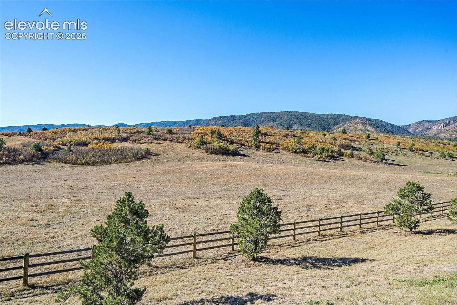 Expansive acreage featuring rolling terrain, split-rail fencing, native trees, and mountainous topography