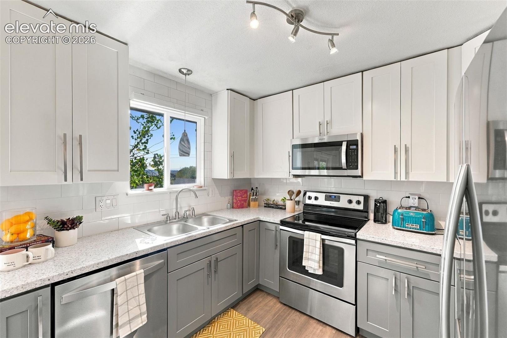 Modern kitchen featuring two-tone cabinetry, stainless steel appliances, a subway tile backsplash, and speckled countertops