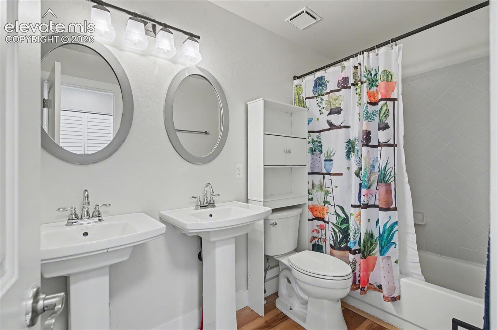 Bathroom featuring dual pedestal sinks, oval-shaped wall mirrors, four-light vanity fixture, and a tub-shower combination with surround tile