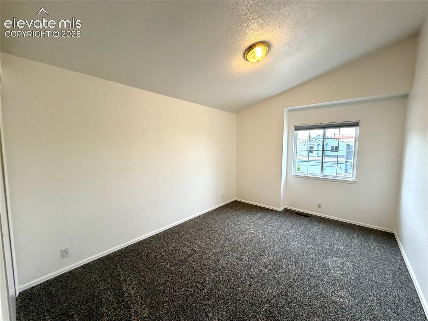 Furniture removed. Spacious guest bedroom with vaulted ceiling and a single window offering natural light