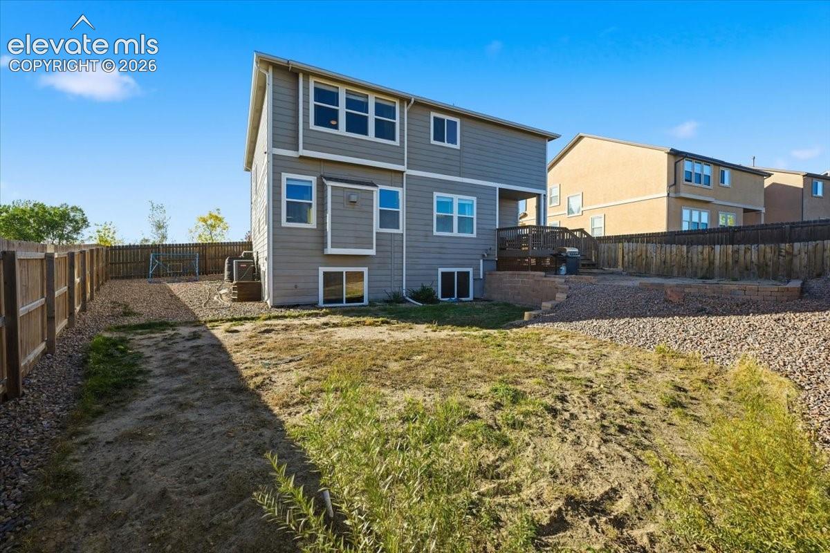 Rear exterior featuring horizontal lap siding, a raised wood deck, a fenced backyard, and stone retaining walls