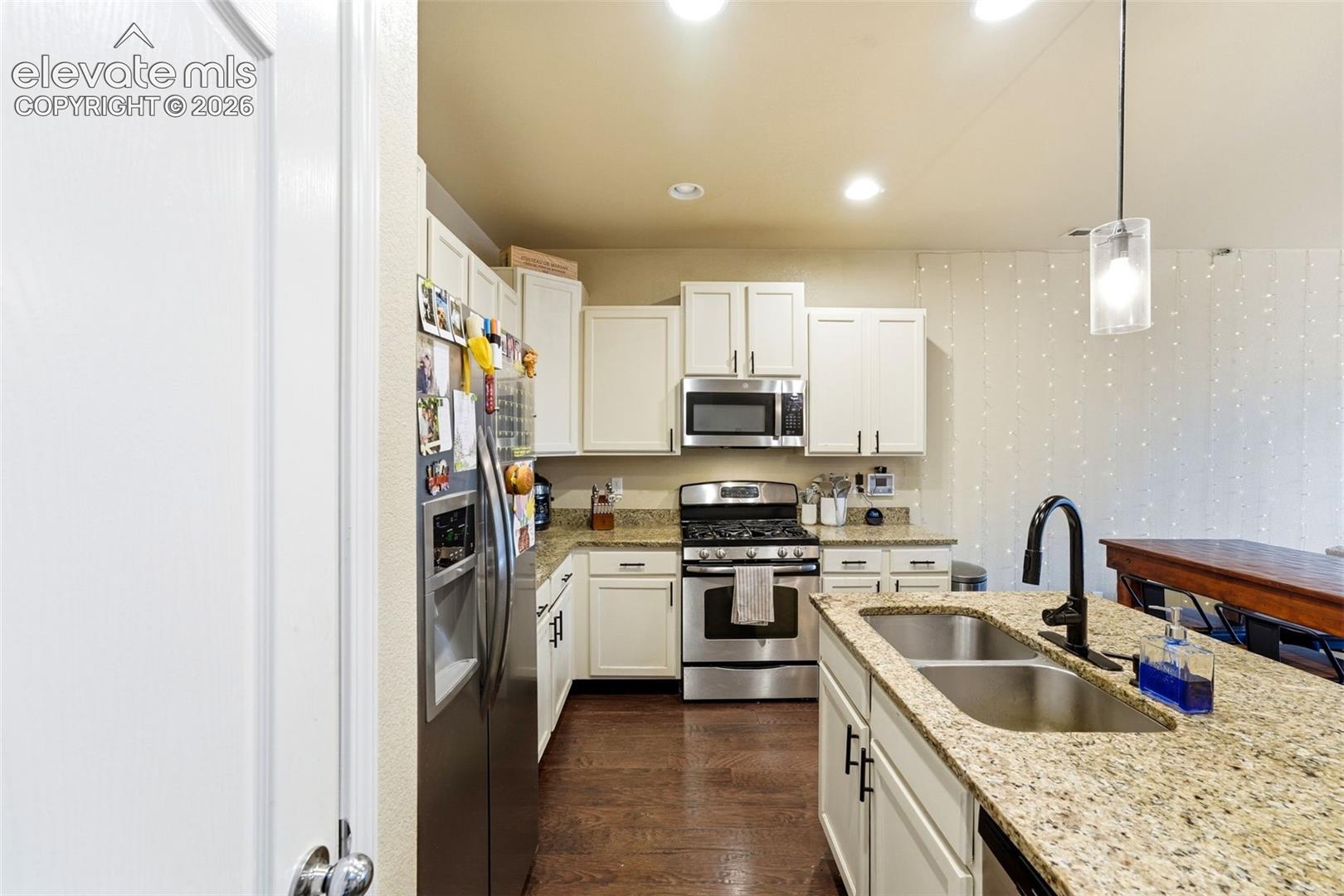 Kitchen featuring white cabinetry, stainless steel appliances, speckled countertops, a double basin sink with a gooseneck faucet, and wood-finish flooring
