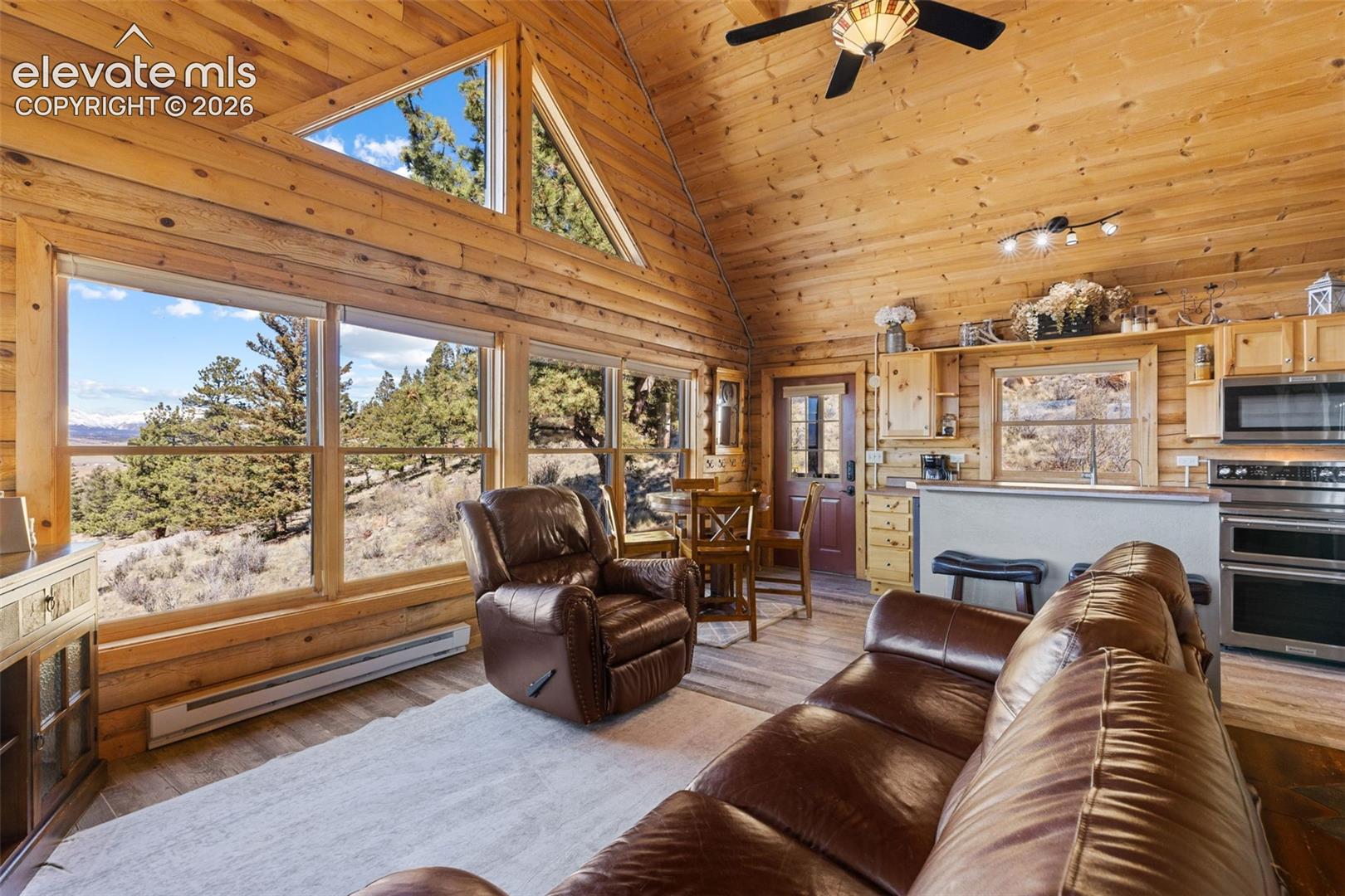 Vaulted ceiling with exposed wood beams, extensive natural log walls, expansive floor-to-ceiling windows, triangular clerestory windows, and built-in wood cabinetry