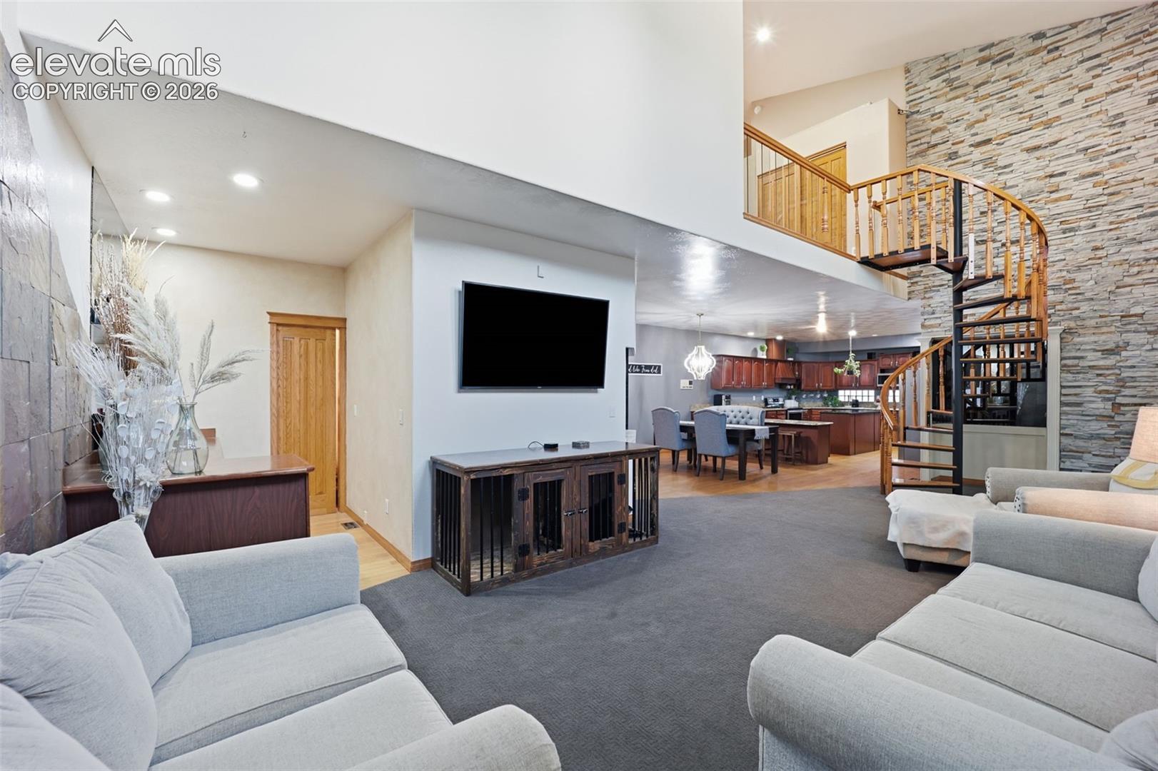 High ceilings, spiral staircase with wood treads, stone accent wall, wood-finish flooring, and recessed lighting