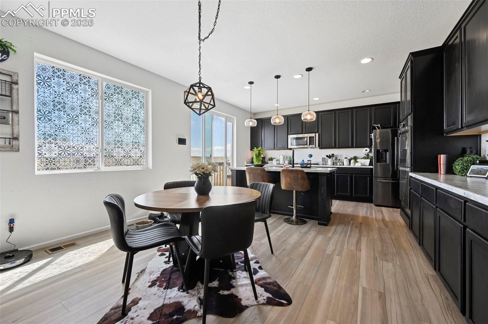 Open-concept kitchen and dining area featuring dark cabinetry with light countertops, wood-finish flooring, and recessed lighting