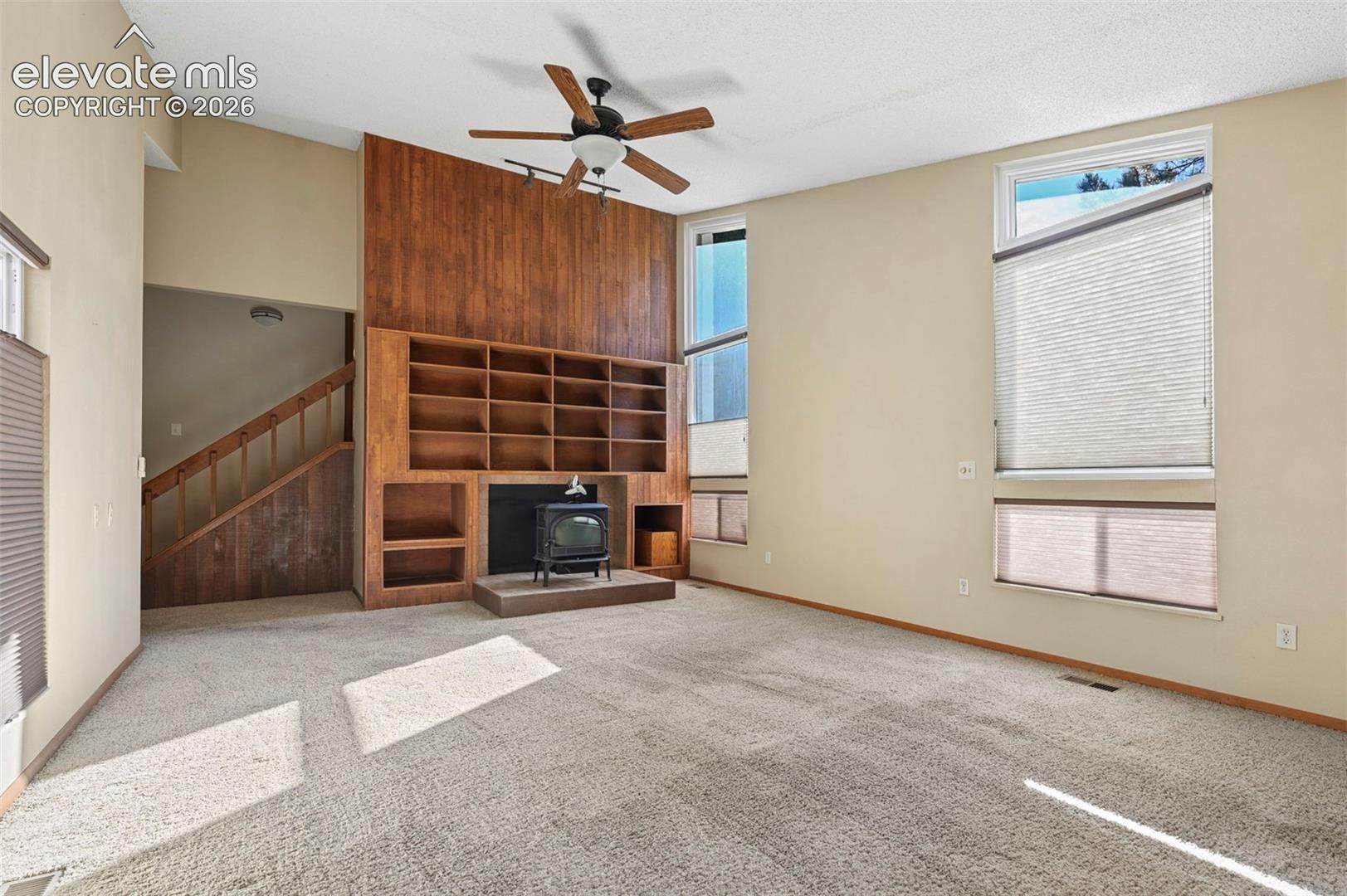 Vaulted ceilings featuring a wood-paneled accent wall, built-in shelving, a freestanding cast-iron stove on a raised hearth, and expansive windows