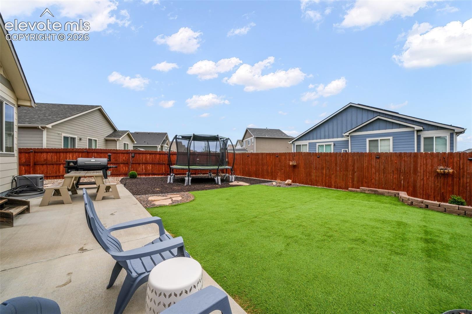 Expansive backyard featuring a concrete patio, artificial turf lawn, and a wood privacy fence