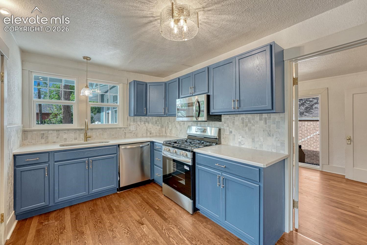 Kitchen featuring blue cabinetry, light countertops, a tile backsplash, stainless steel appliances, and wood-finish flooring