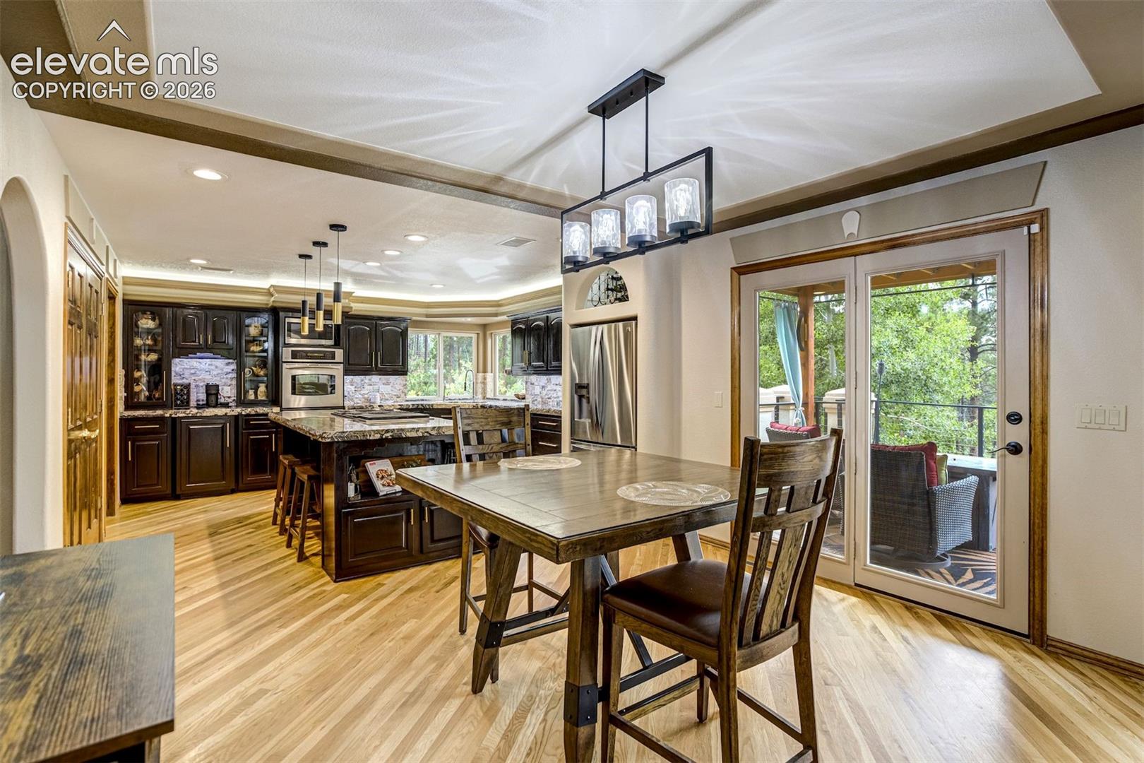 Hardwood-style flooring, tray ceiling with recessed lighting, black cabinetry with glass-front accents, stainless steel built-in appliances, and double glass doors