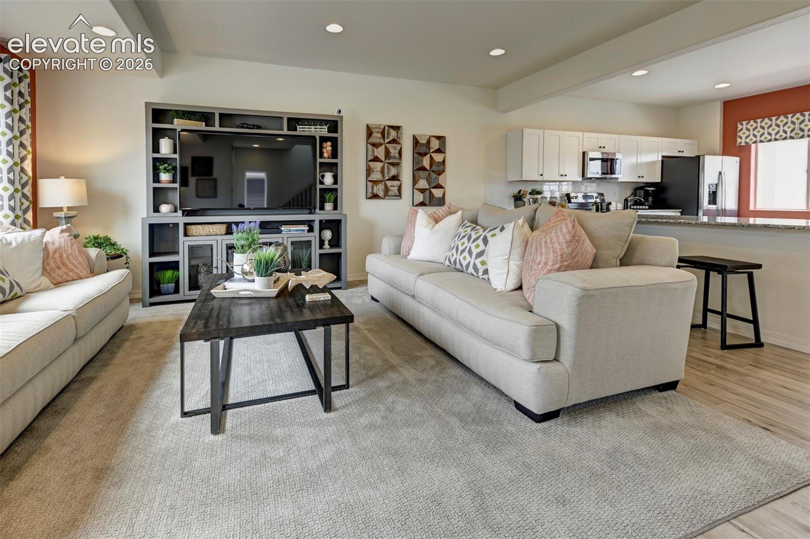 Living room with built-in TV shelving and adjacent open kitchen with white cabinets and breakfast bar