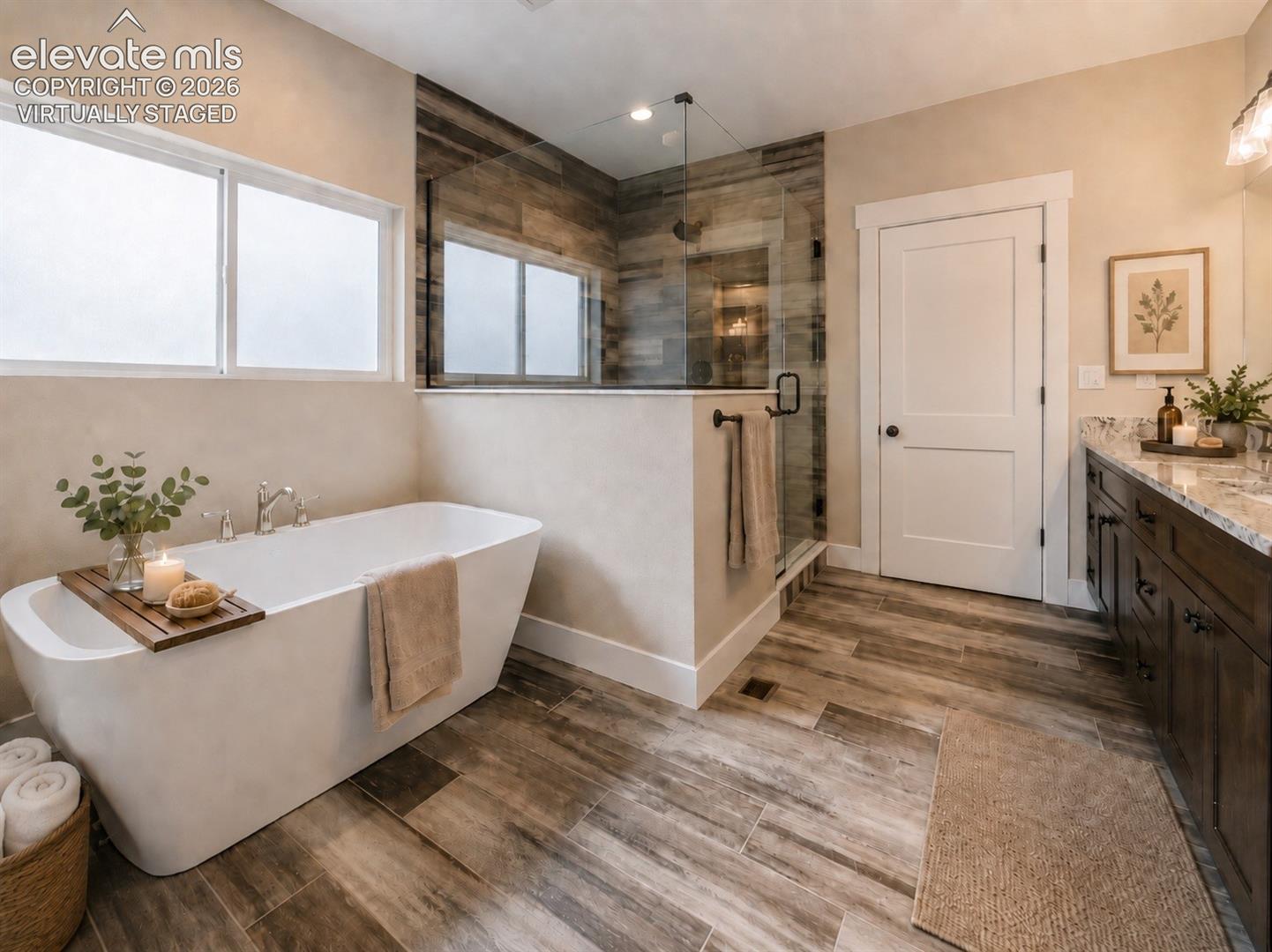 Virtually Staged Freestanding tub with dual windows, glass-enclosed shower with wood-finish tile, double vanity with stone countertop, and wood-finish plank flooring