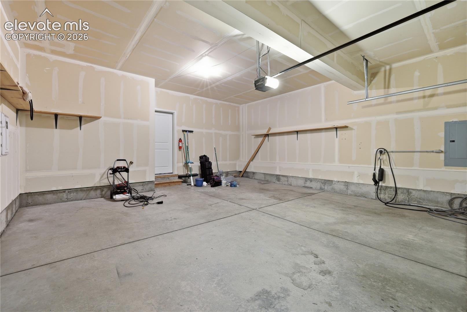 Spacious garage featuring a concrete floor, built-in shelving, an overhead garage door opener, a utility door, and an electrical service panel