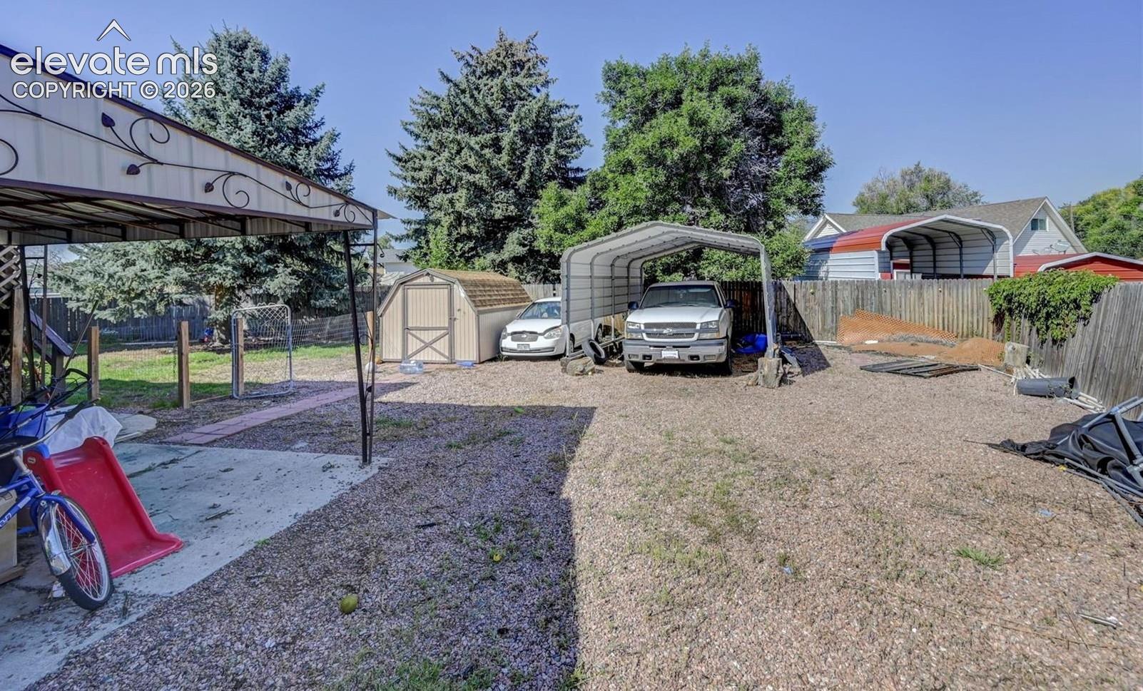 Gravel backyard featuring a metal-frame carport, a detached storage shed, a concrete patio, and wood privacy fencing