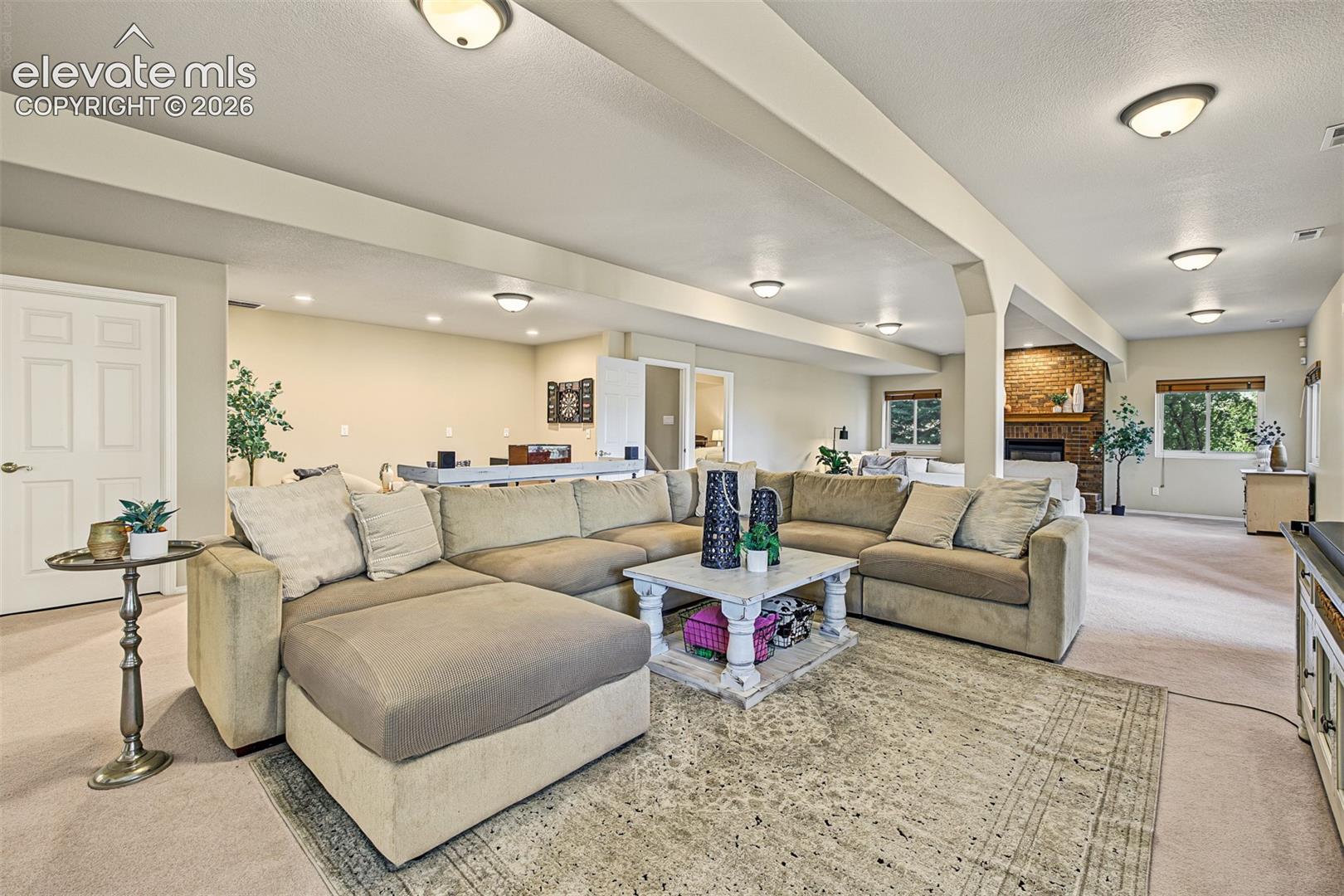 Spacious family room in the full walkout basement, featuring an expansive open layout, comfortable seating area, neutral carpeting, and a gas-burning fireplace with brick surround.