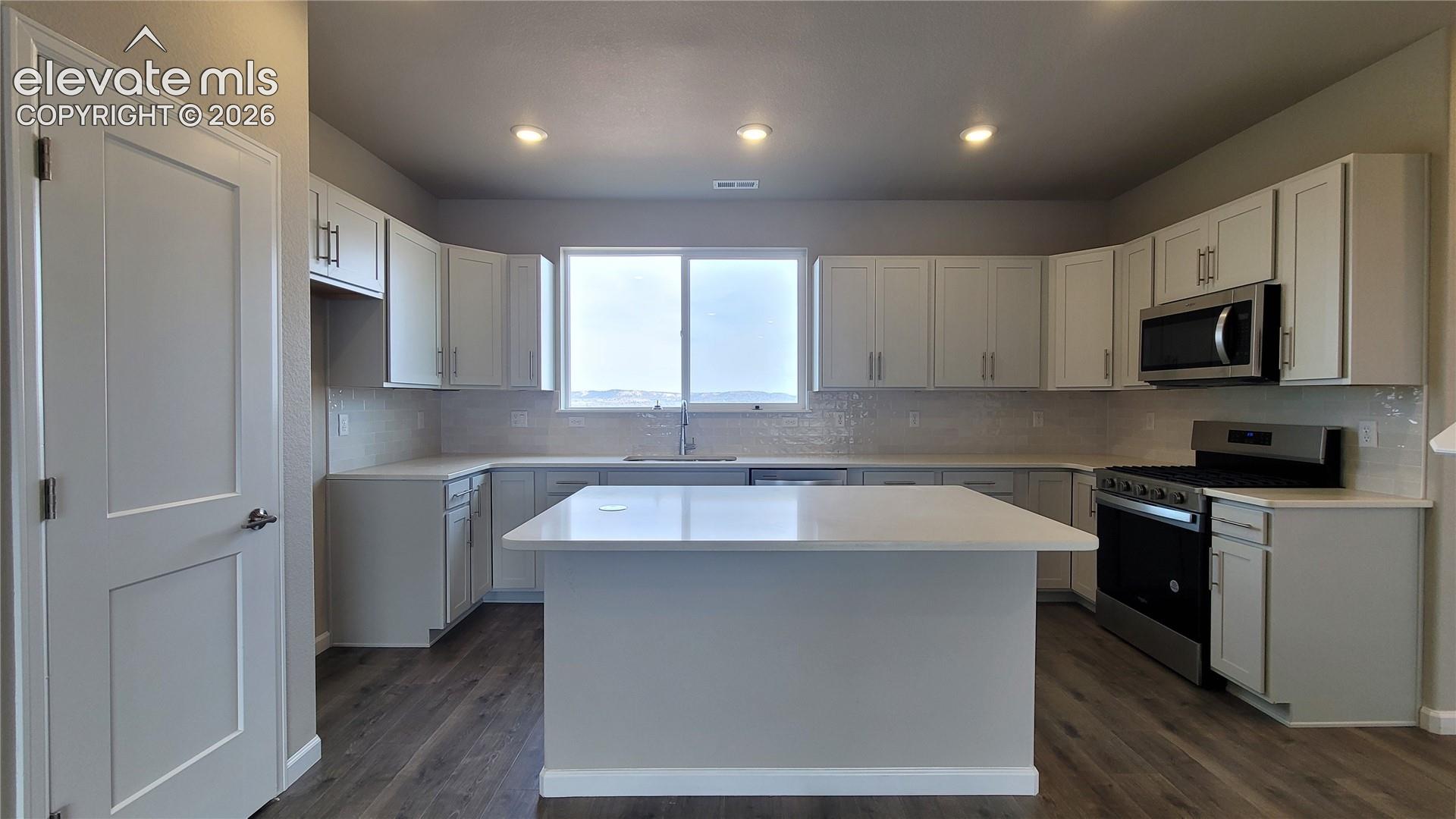 Kitchen with quartz countertops, pantry, large island providing additional seating, and stainless steel gas range, microwave, and dishwasher! 
