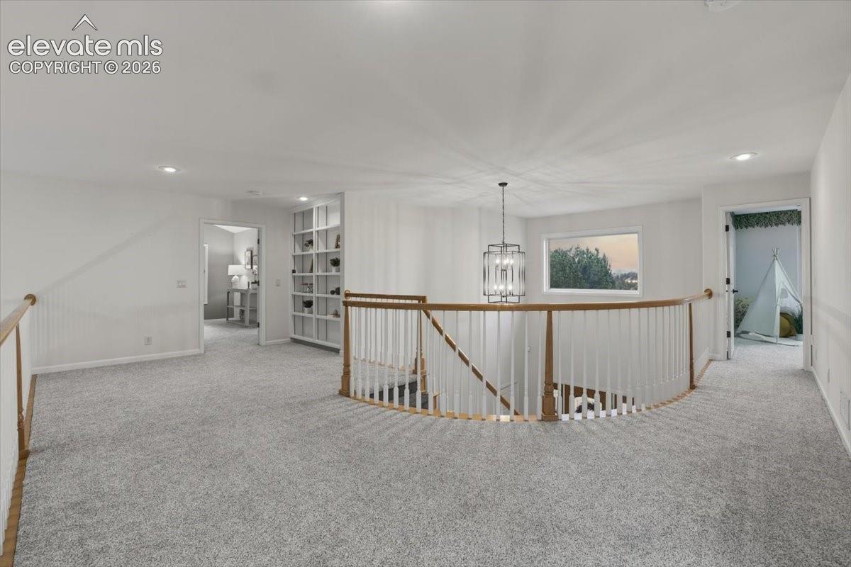 Open landing featuring light gray carpeting, a curved staircase with a wood handrail, recessed lighting, and a modern chandelier