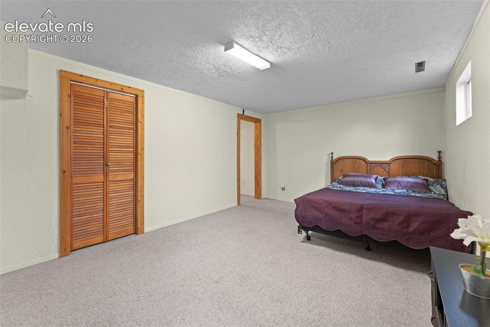 Spacious room with light-colored carpeting, wood-frame louvered bi-fold closet doors, and recessed window