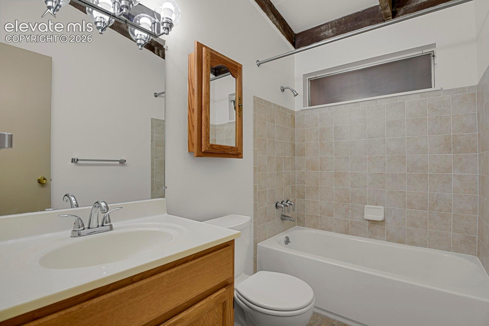 Bathroom featuring wood-finish cabinetry, a white vanity countertop with an integrated sink, a tiled shower surround, a wall-mounted medicine cabinet, and exposed ceiling beams