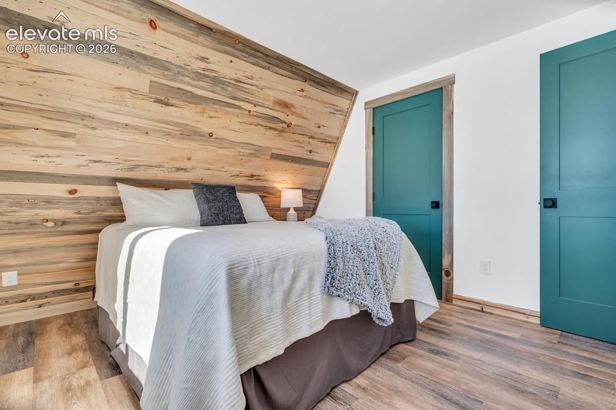 Wood-plank accent wall featuring an angled ceiling line, teal-painted interior doors with matte black hardware, and wood-finish flooring