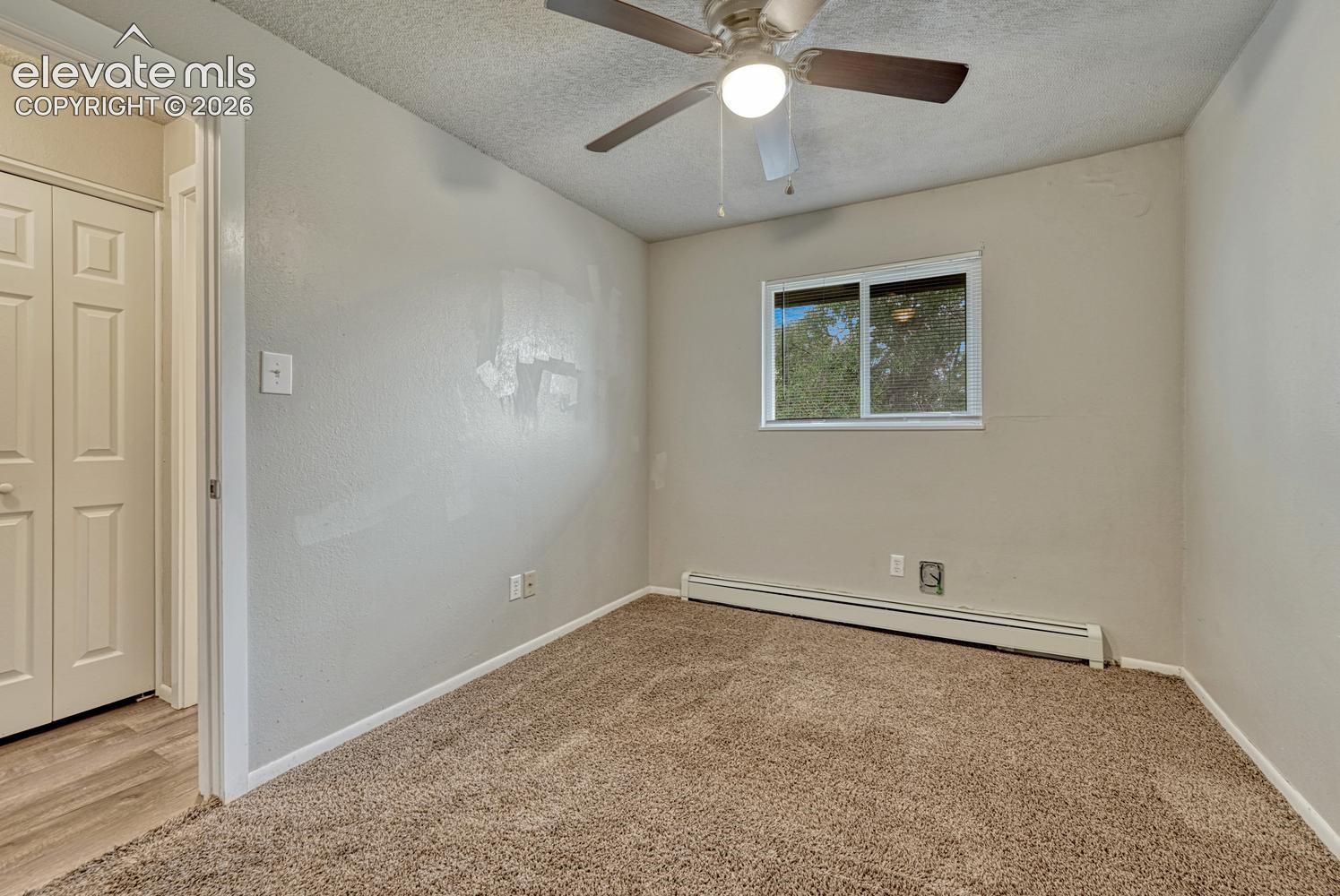 Carpeted room featuring a ceiling fan with integrated lighting, a double-paned window, baseboard heating, and a bi-fold closet door