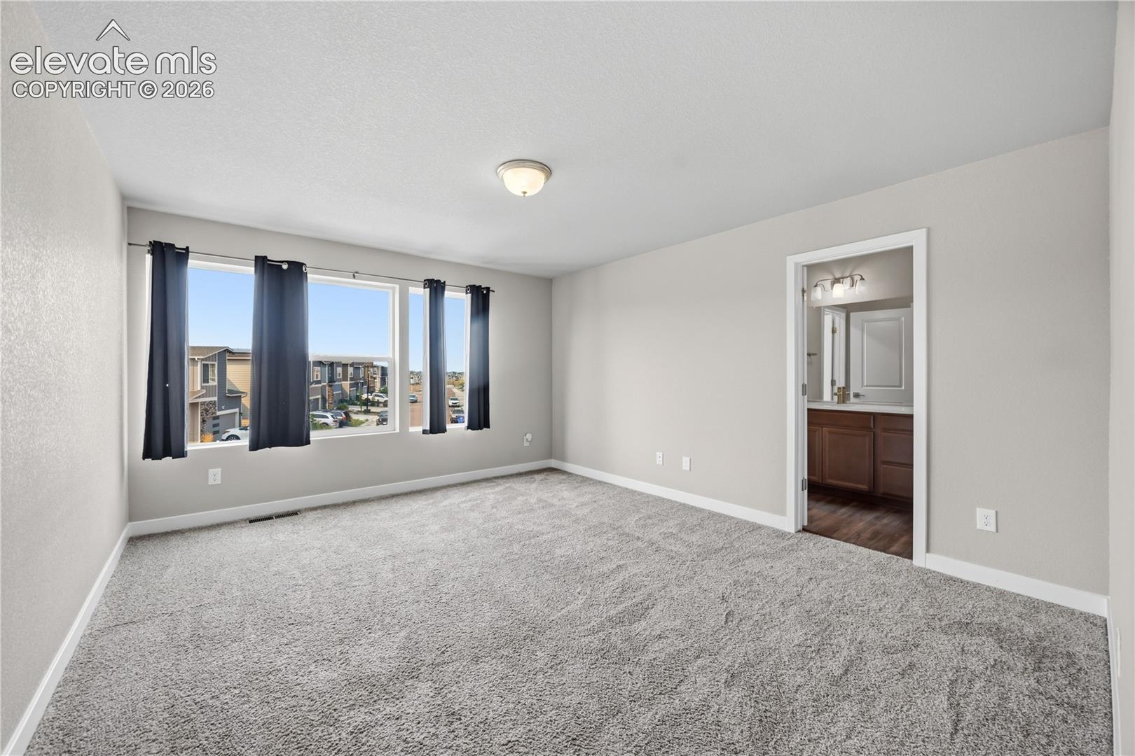 Spacious upper level Primary Retreat with neutral carpet, a wall of windows, adjoining bathroom, and walk in closet.
