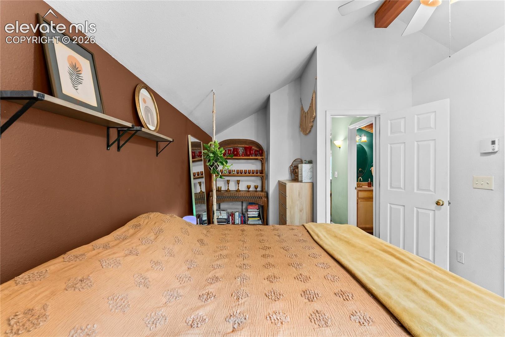 Vaulted ceilings featuring an exposed wooden beam, wall-mounted shelving unit, and a multi-panel interior door