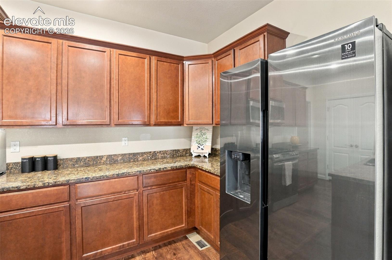 Kitchen featuring stained wood cabinetry, stone-surface countertops, and a stainless steel side-by-side refrigerator