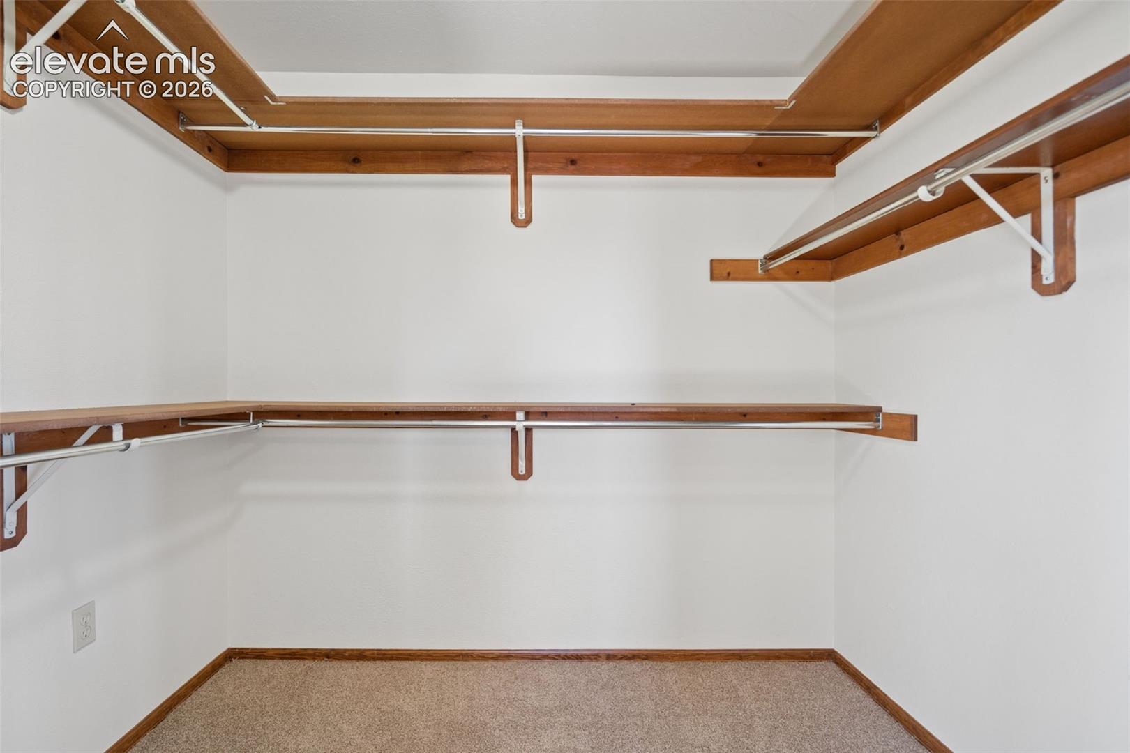 Built-in shelving with hanging rods and neutral carpet flooring