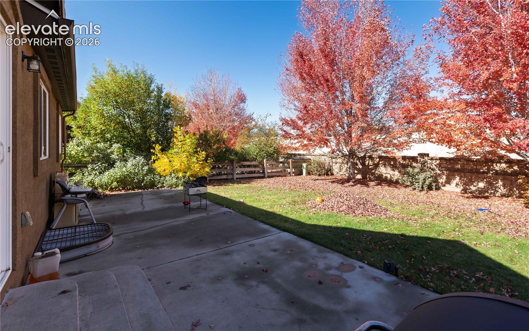 Backyard featuring a concrete patio, grassy lawn, wood-style perimeter fencing, and mature deciduous trees