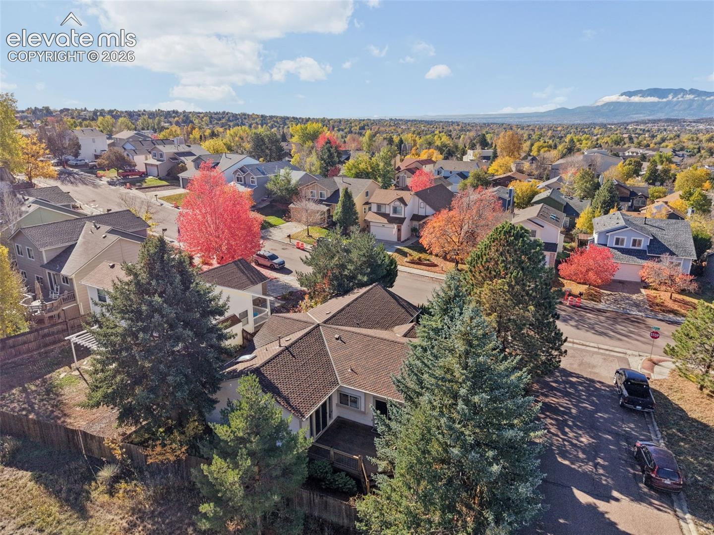 Aerial perspective featuring a shingled roof, elevated rear deck, and mature evergreen trees against a mountainous backdrop