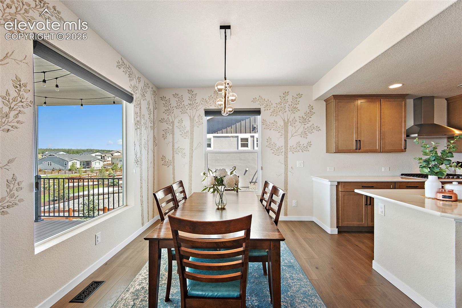 Expansive window, wood-finish flooring, contemporary pendant lighting, kitchen cabinetry, and stainless steel range hood