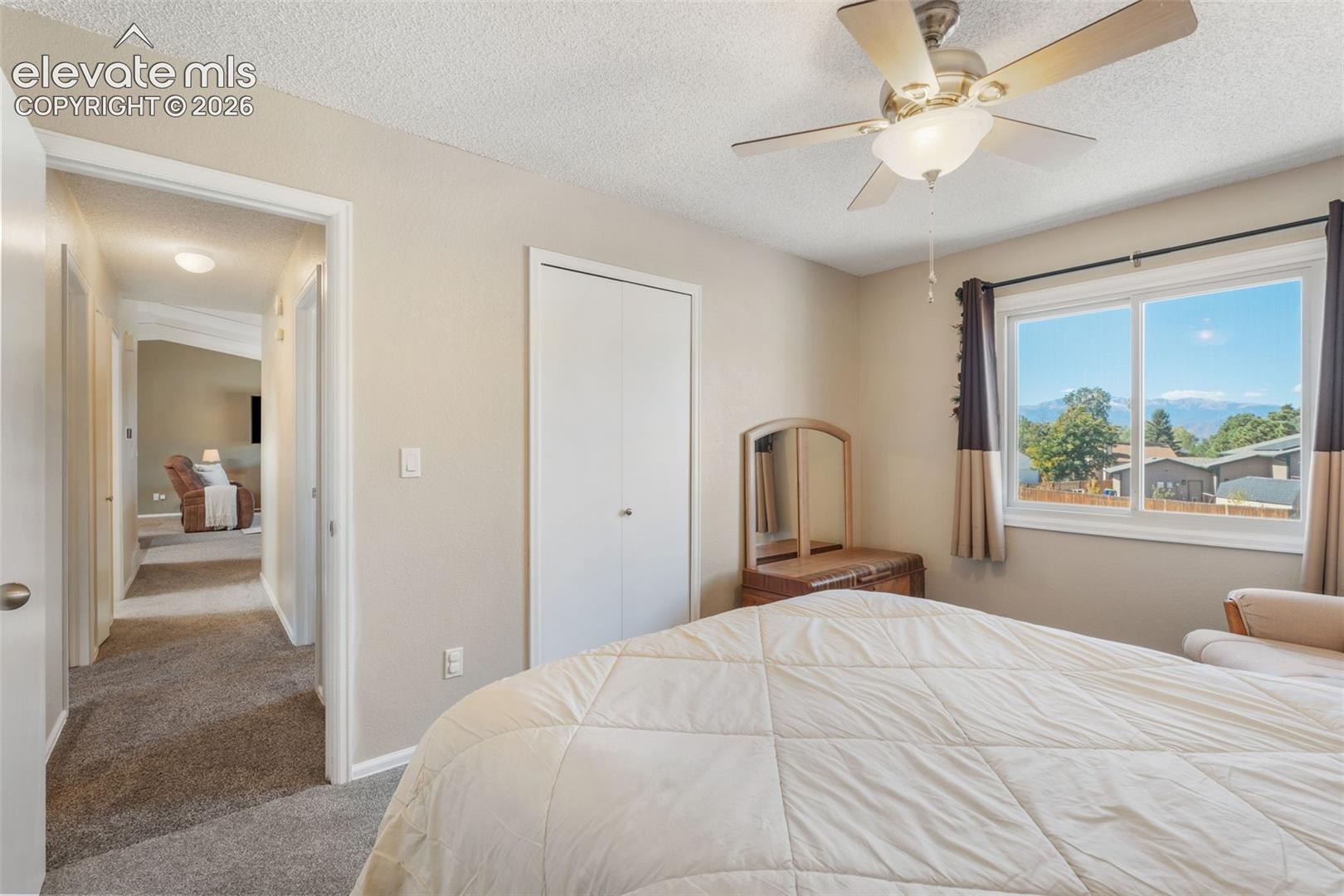 Neutral-toned room featuring a ceiling fan with integrated lighting, wall-to-wall carpeting, dual-door closet, and window with a mountain backdrop