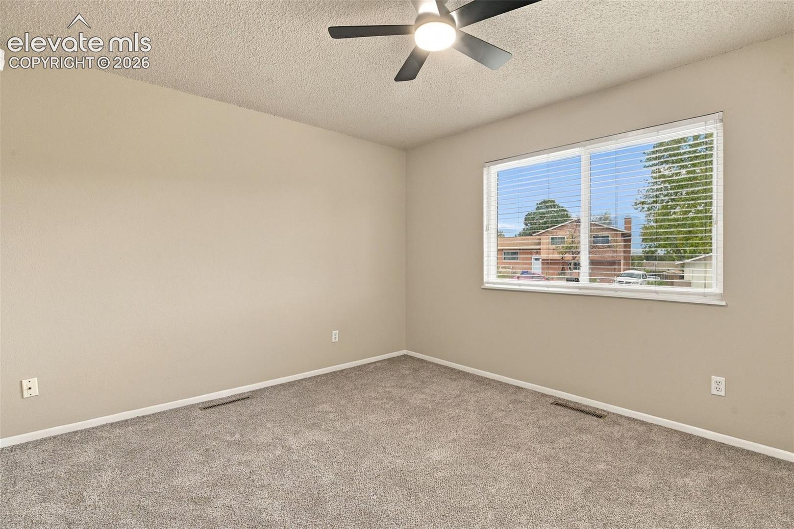 Interior room featuring neutral wall paint, wall-to-wall carpeting, a large dual-pane window with installed blinds, and a ceiling-mounted light fixture with a fan