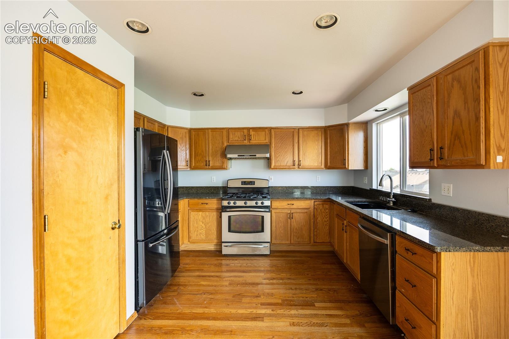 Kitchen featuring wood-finish flooring, recessed lighting, wood cabinetry, dark countertops, and stainless steel appliances