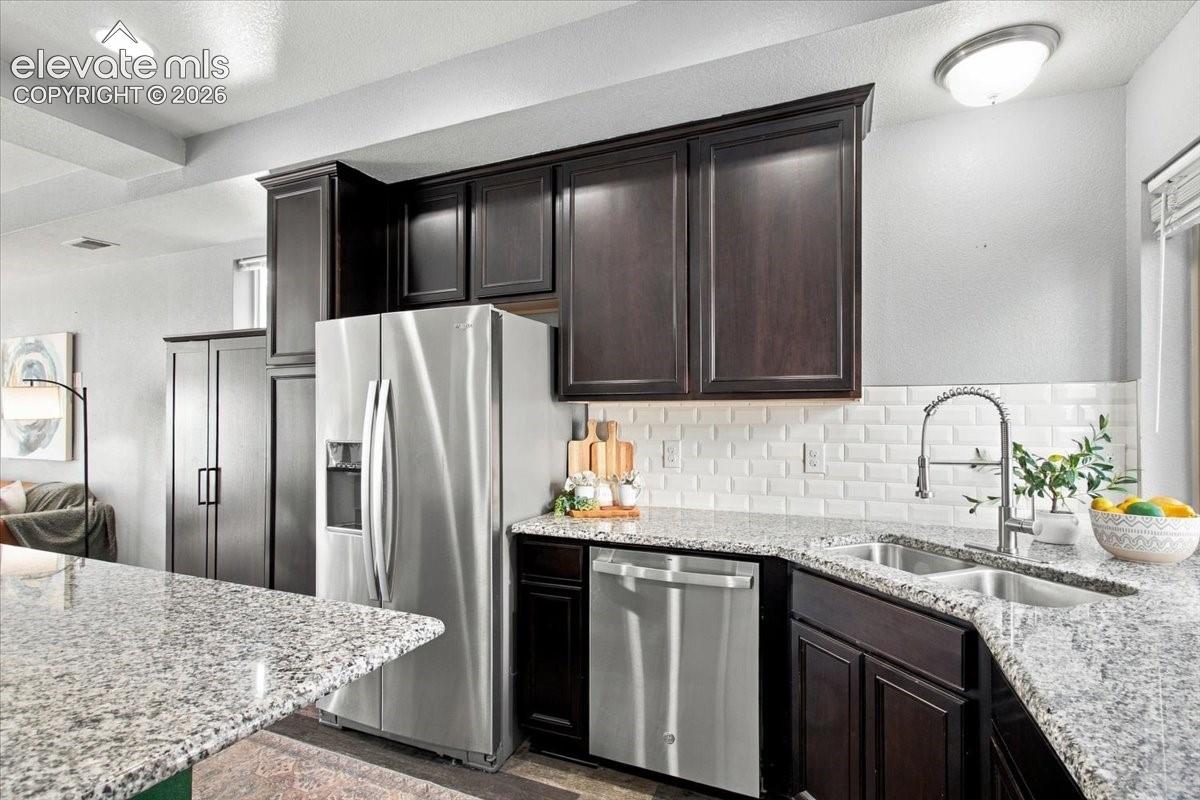Modern kitchen featuring dark cabinetry, stainless steel appliances including a side-by-side refrigerator and dishwasher, white subway tile backsplash, and light-colored quartz countertops with waterfall island seating