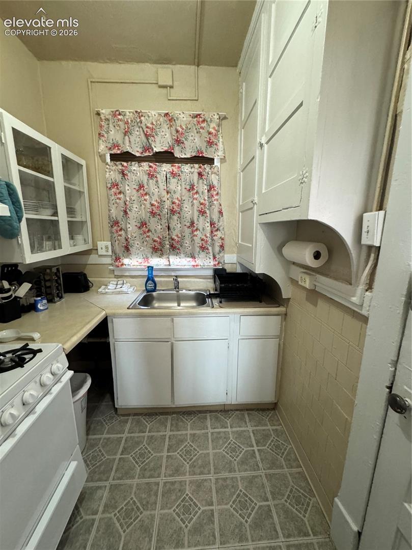 Compact kitchen featuring a stainless steel sink, white cabinetry, and patterned flooring