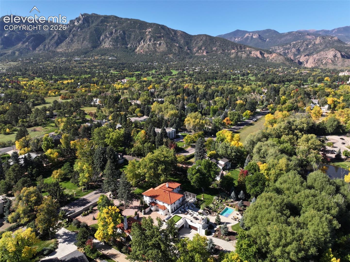 Aerial perspective featuring a multi-story residence with a red tile roof, an in-ground swimming pool, stone-paved hardscaping, and mountain backdrop