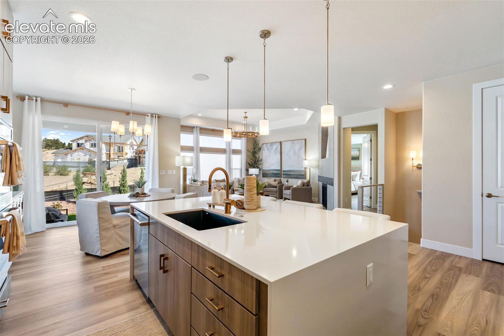 Kitchen island featuring a white countertop, undermount sink with a gold-tone faucet, and wood-finish cabinetry with matte hardware, complemented by pendant lighting and wood-finish flooring