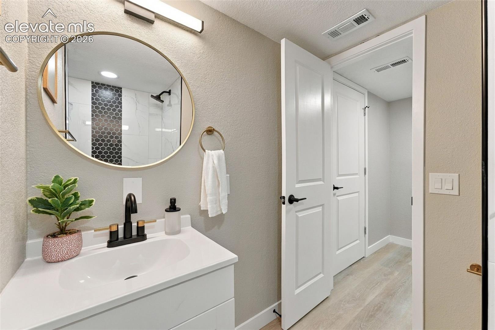 White vanity cabinet with an integrated basin, matte black faucet, gold-trimmed oval wall mirror, and wood-finish flooring