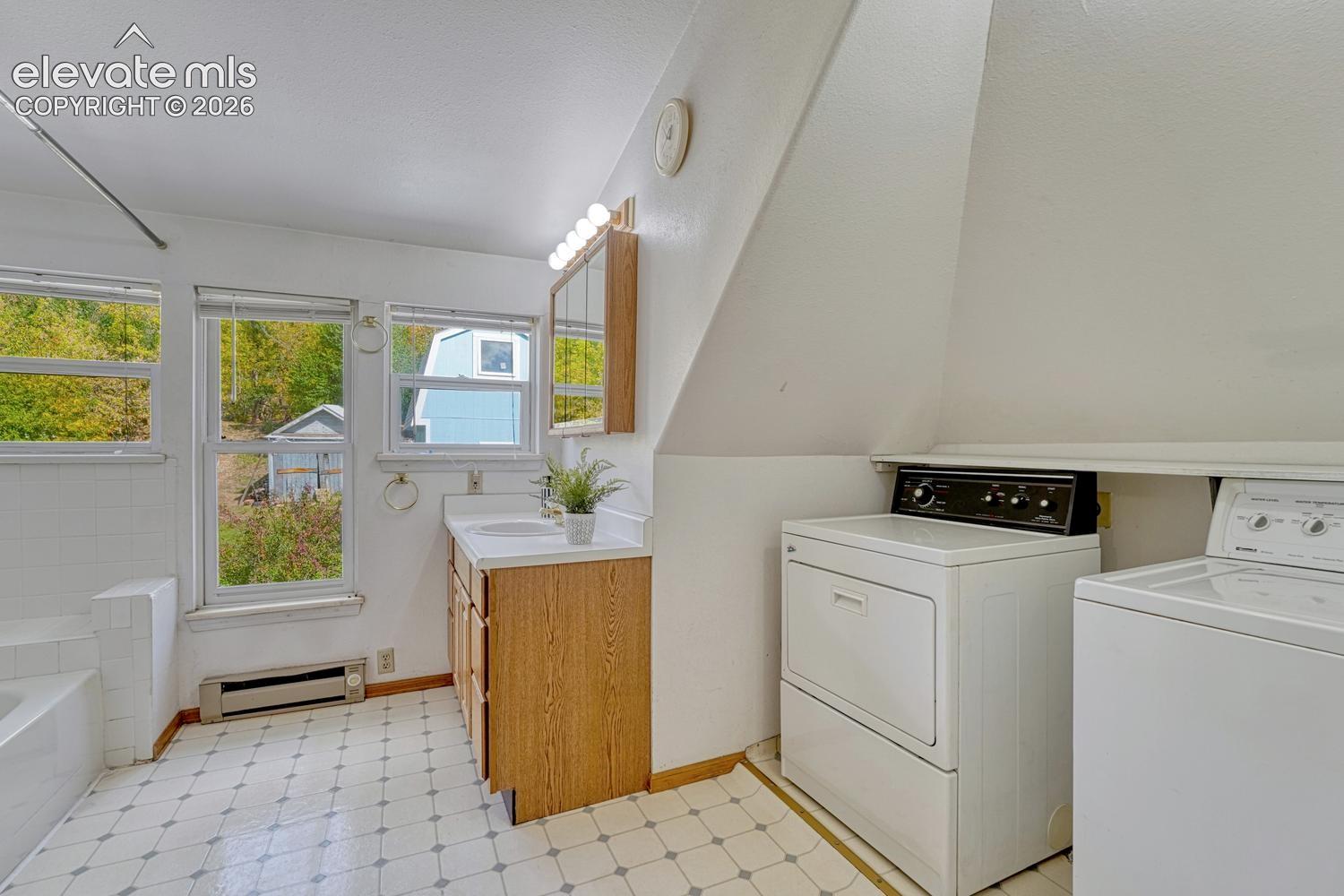 White tiled flooring, dual windows, wood-finish vanity with a built-in sink, and a built-in laundry area