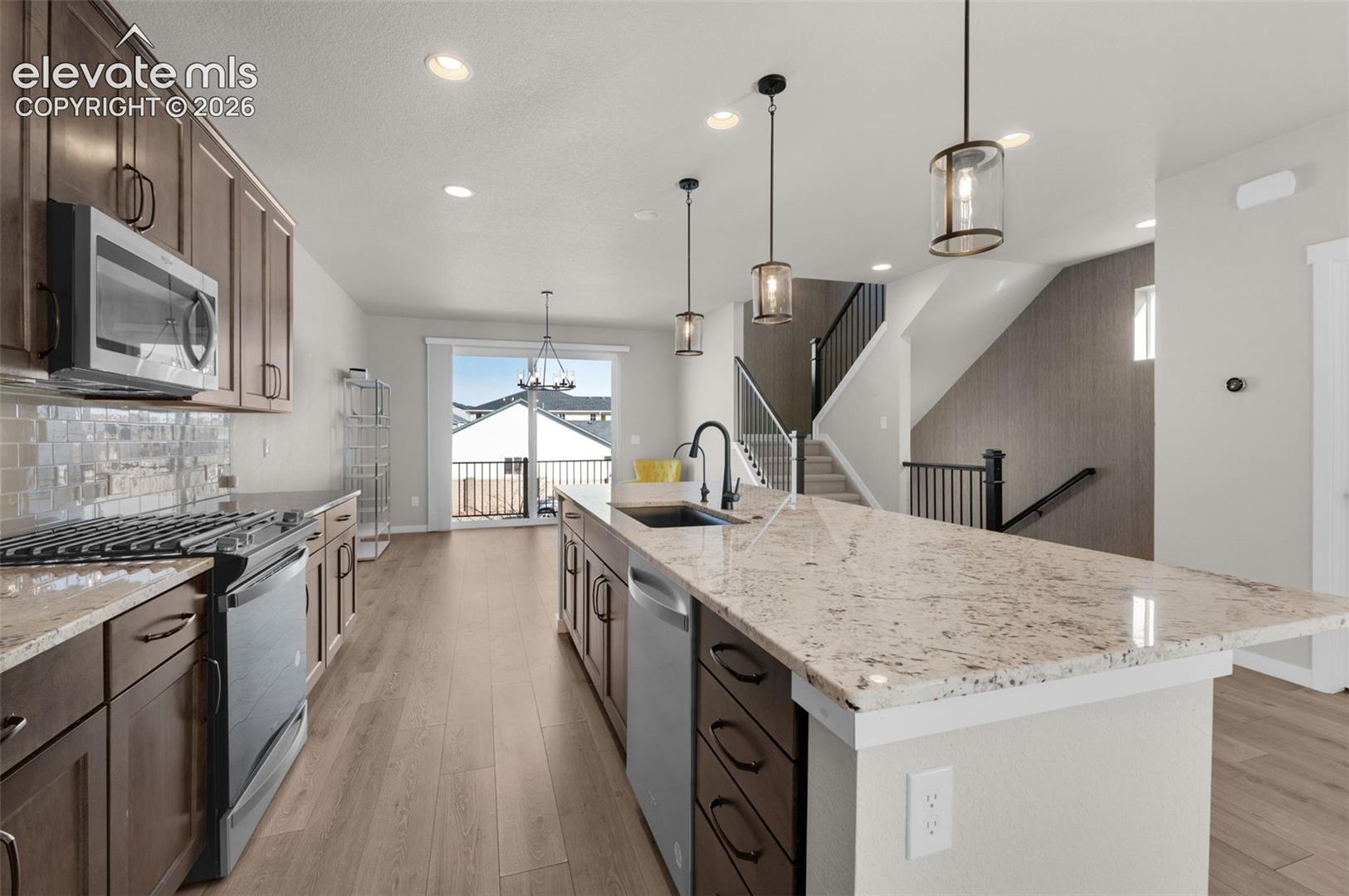 Open-concept kitchen featuring an island with a built-in sink, stainless steel appliances, wood-finish flooring, recessed lighting, and a glass tile backsplash