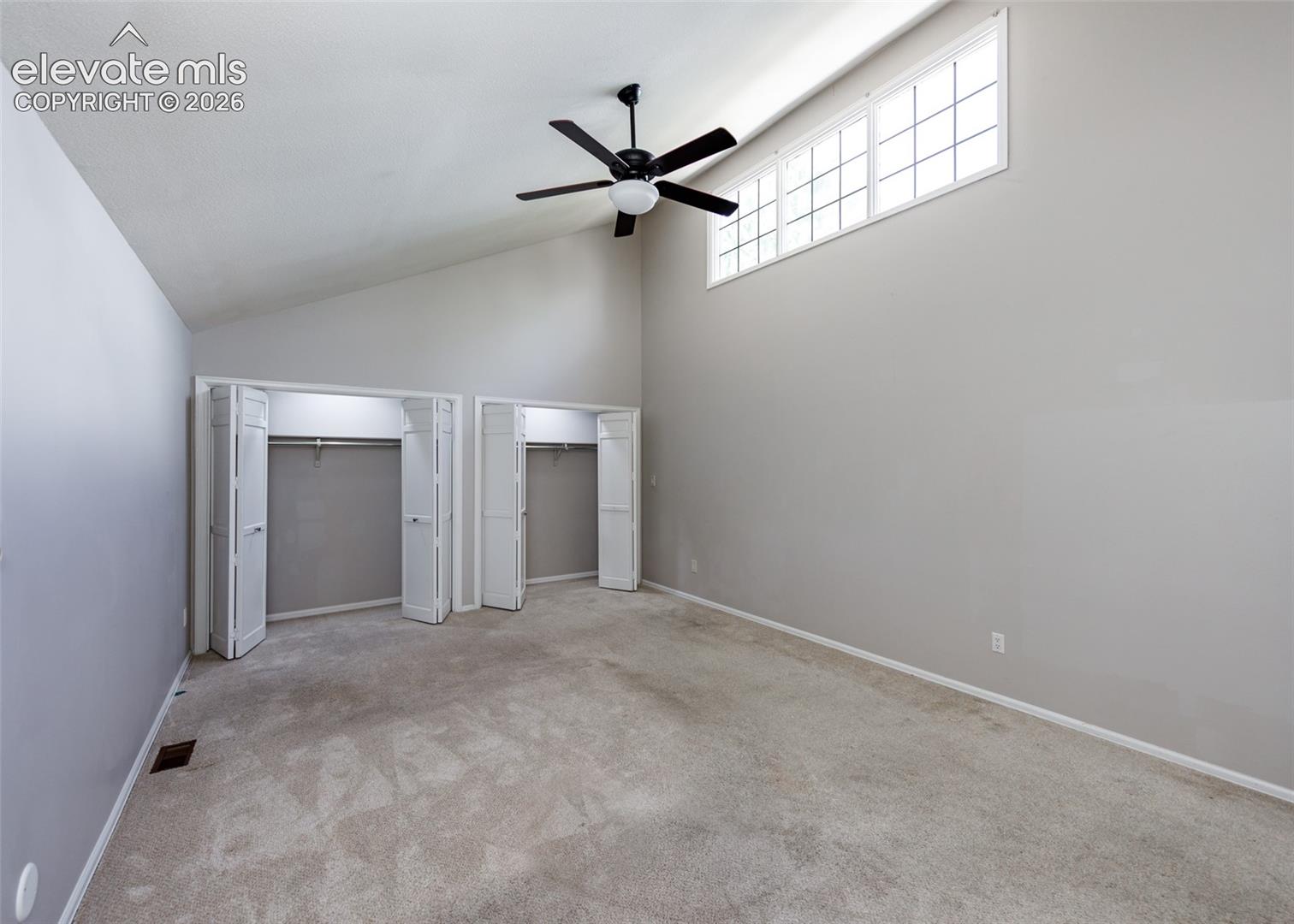 Vaulted ceiling with an integrated ceiling fan, transom windows, and built-in bifold door closets