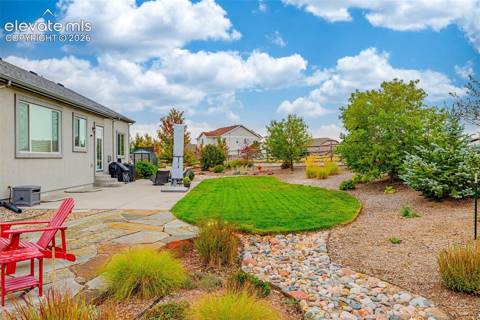 Stucco exterior featuring a flagstone patio, manicured lawn, decorative rock drainage bed, and native landscaping