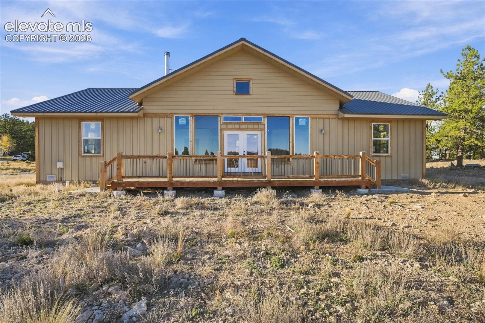 Single-story residence featuring vertical siding, a metal roof, a full-length wood deck, and double-entry glass doors