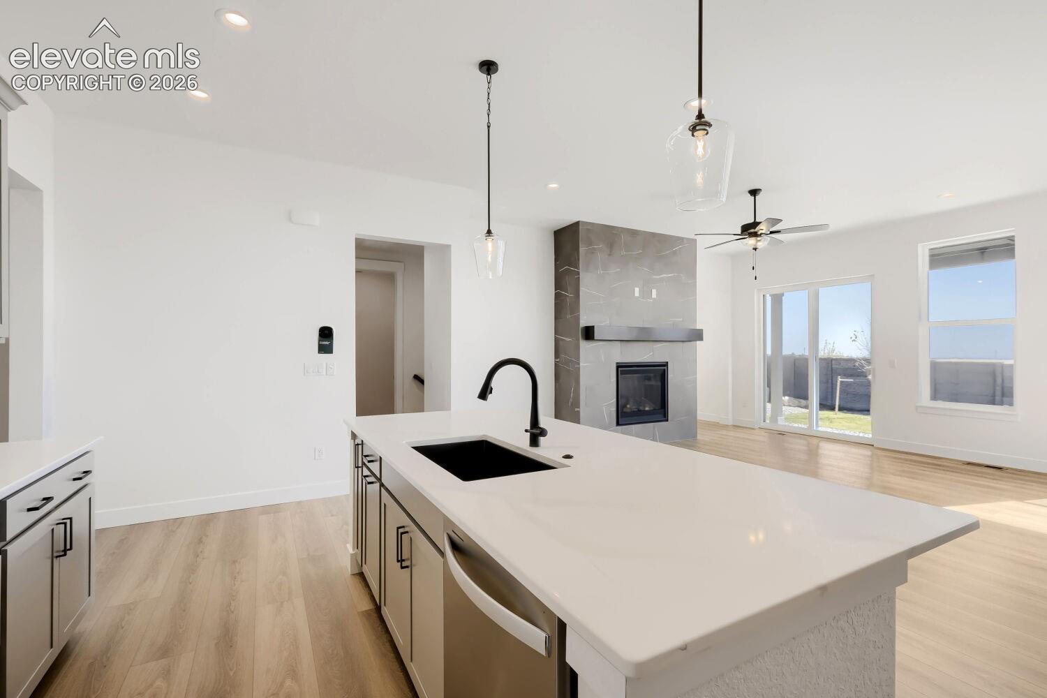 Kitchen island with a built-in sink, stainless steel dishwasher, and pendant lighting