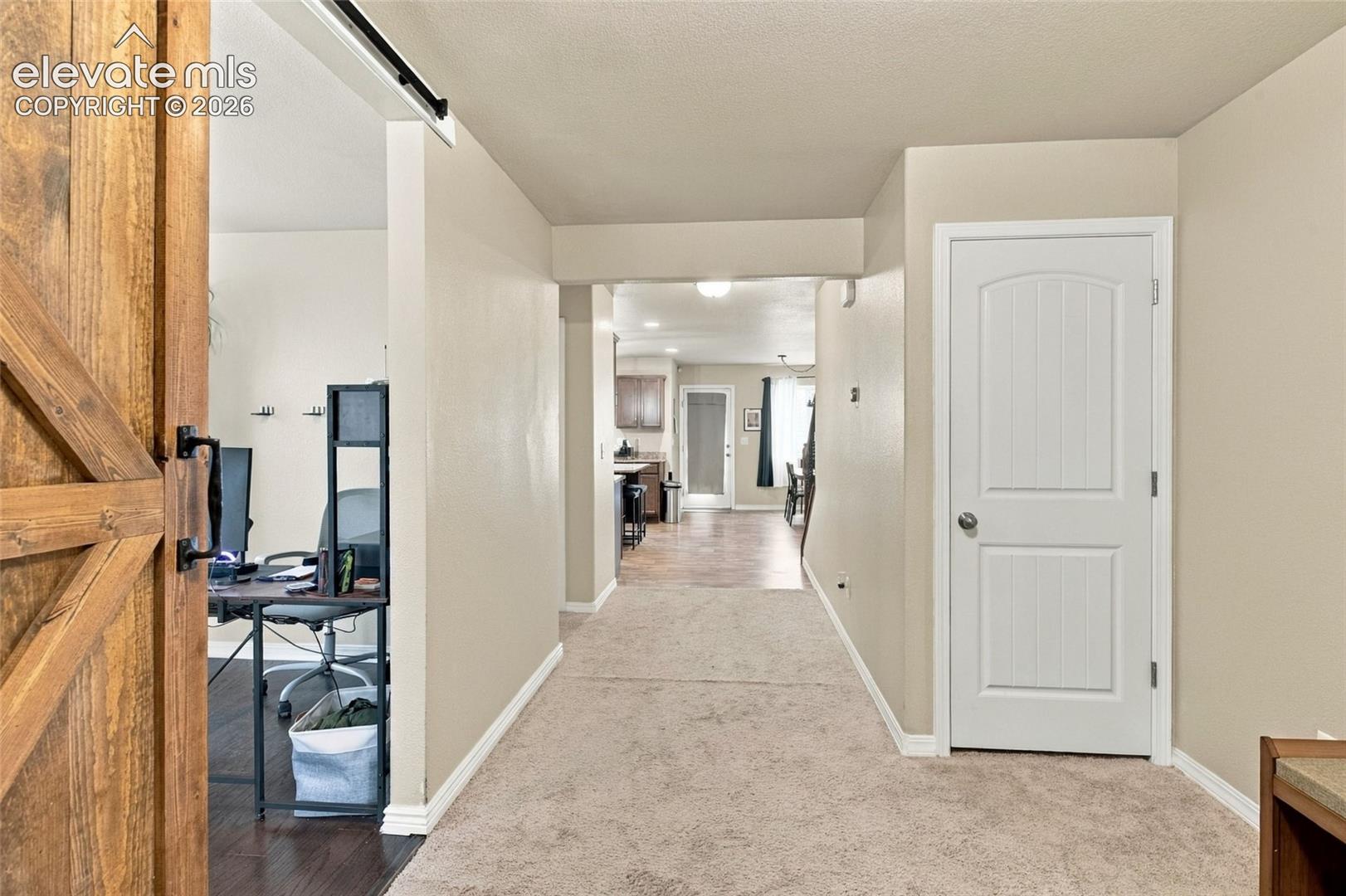 Interior hallway featuring neutral carpeting, a wood-finish sliding barn door with matte black hardware, and a white two-panel interior door